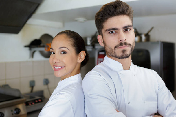 male and female chefs back to back in professional kitchen - Foto, afbeelding