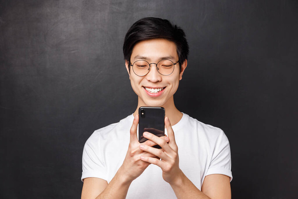 Teknologia, viestintä ja ihmisten käsite. Lähikuva muotokuva iloinen nuori aasialainen mies hymyilee matkapuhelin, katsella video internetissä, saavat hyviä uutisia sähköpostitse, musta tausta
 - Valokuva, kuva
