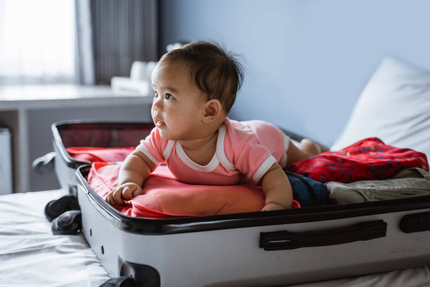 asian baby smiles on his stomach in an open suitcase - Foto, Imagen