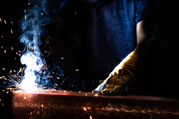 Metalen lasser werken met boog lassen machine om staal te lassen in de fabriek terwijl het dragen van veiligheidsuitrusting. Metaalbewerking en onderhoud van de bouw door middel van handenarbeid concept. - Foto, afbeelding