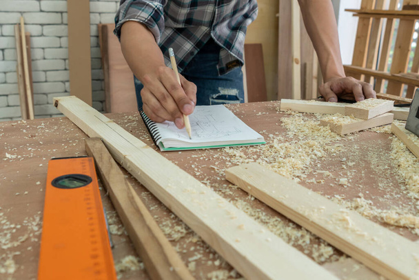 Asztalos dolgozik fa kézműves műhelyben, hogy készítsen építőanyagot vagy fabútorokat. A fiatal ázsiai ácsok professzionális eszközöket használnak a kézművességhez. DIY asztalos és asztalos munka koncepciója. - Fotó, kép