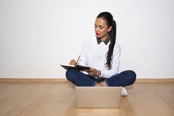 fiatal nő gazdaság notebook és toll mellett ül laptop - Fotó, kép