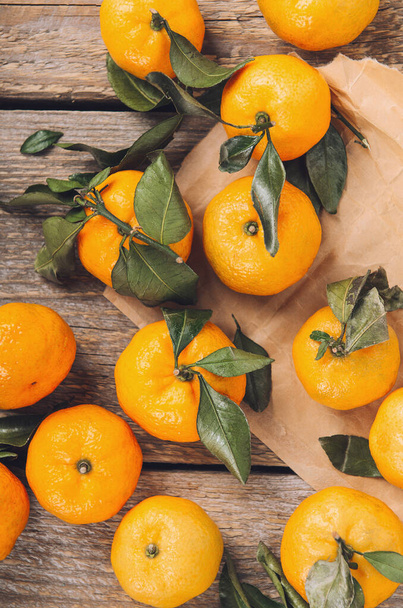 A pile of fresh sweet mandarins with green leaves on a wooden table on craft paper. top view, flat lay - Foto, Imagem