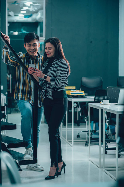 Happy young man and woman in the office smiling and looking at the screen of a modern smartphone - Photo, image