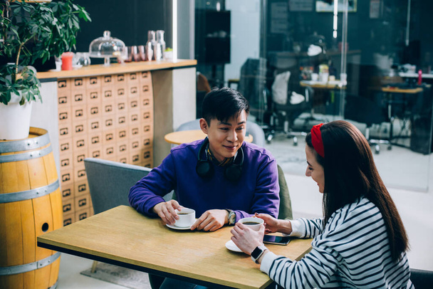 Gladsome young lady smiling while drinking coffee with a young man - 写真・画像
