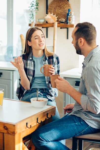 Young man drinking tea and a young lady gesturing while talking to him - Foto, Imagem