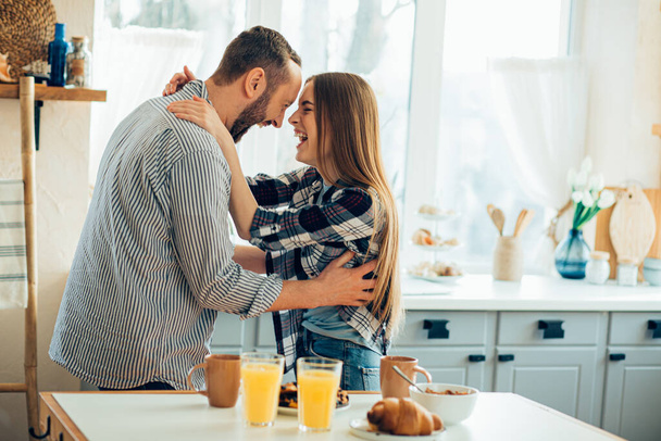 Positive young man and woman hugging and smiling in excitement while being in the kitchen - Photo, Image