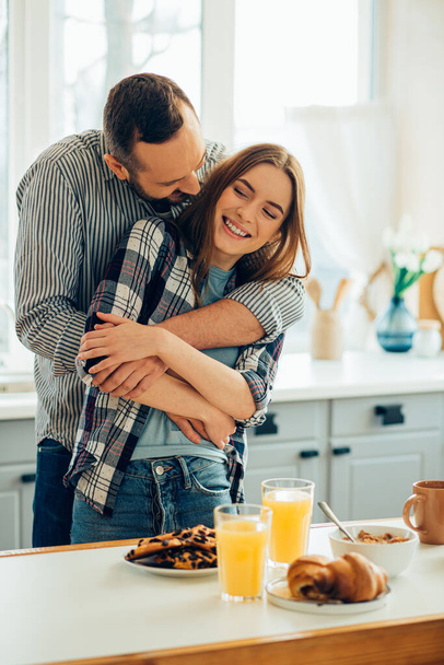 Beautiful lady smiling while a boyfriend hugging her. Tasty breakfast on the table - Foto, Bild