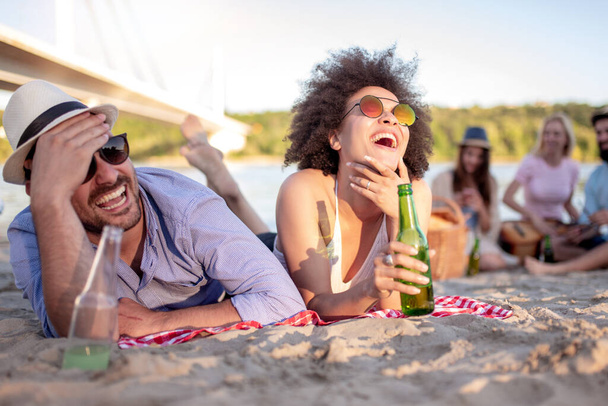 Young beautiful couple having fun on the beach, drinking beer and smiling. - 写真・画像