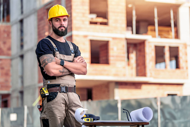 Portret męskiego architekta na placu budowy ze skrzyżowanymi ramionami, patrzy w kamerę. - Zdjęcie, obraz