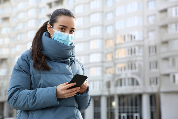 Woman with disposable mask and smartphone outdoors. Dangerous virus - Photo, Image