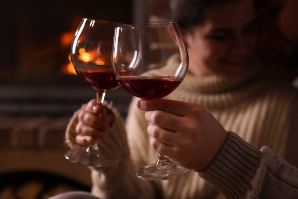 Kedves pár egy pohár borral közel kandalló otthon, összpontosítson a kezét. Téli vakáció - Fotó, kép