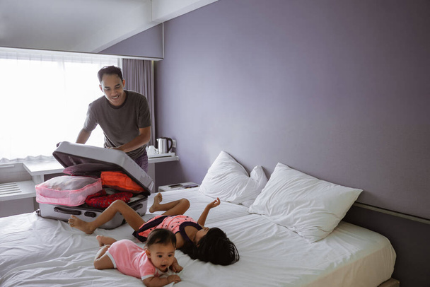 father is preparing the suitcase when his two children play on the bed - Foto, imagen