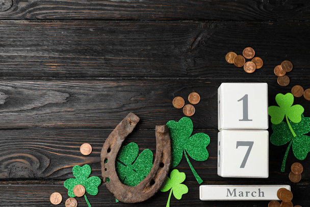 Flat lay composition with horseshoe and block calendar on black wooden background, space for text. St. Patrick's Day celebration - 写真・画像