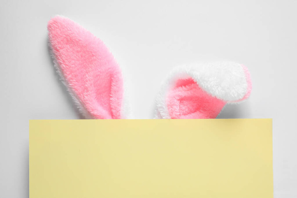 Decorative bunny ears and yellow card on white background, top view. Easter holiday - Foto, afbeelding