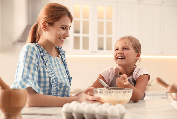 Mother and daughter making dough together in kitchen - Фото, изображение