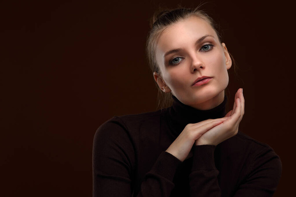 Studio portrait of a beautiful slender girl in a maroon turtleneck on a brown background - Foto, afbeelding