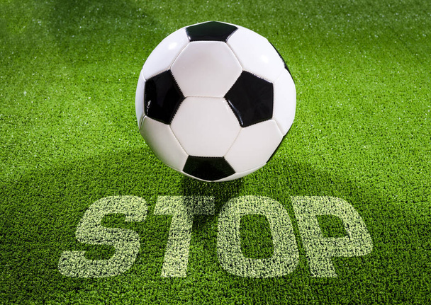 Stoppt das Fußballspiel. Klassischer schwarz-weißer Fußball in einem Stadion, auf dem Rasen steht "Stop". Konzept, die Fußballmeisterschaft zu stoppen. - Foto, Bild