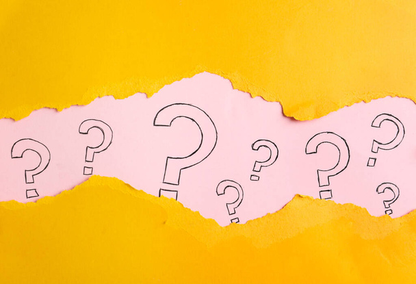 Ερωτηματολόγια σε ροζ φόντο, προβολή μέσα από τρύπα σε κίτρινο χαρτί - Φωτογραφία, εικόνα