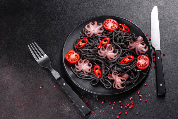 Ζυμαρικά μαύρα θαλασσινά με γαρίδες, χταπόδι και μύδια σε μαύρο φόντο. Μεσογειακό γκουρμέ φαγητό. Μαύρη μακαρονάδα με χταπόδι σε μαύρο πέτρινο πιάτο - Φωτογραφία, εικόνα