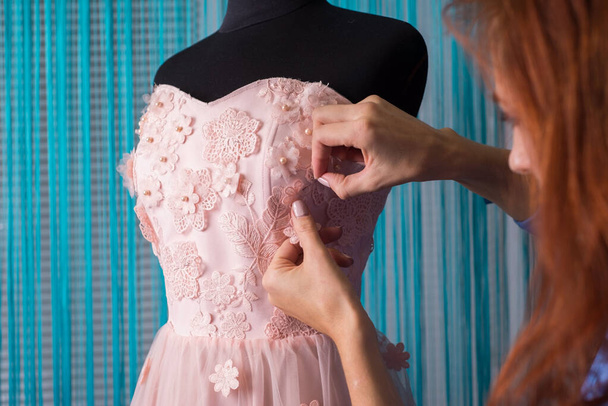 the process of making clothes. Professional designer, handmade craftsman, sews flowers on a pink dress, on a mannequin, in a workshop. Tailoring, women's dress. Pink wedding dress - Фото, изображение
