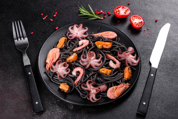 Schwarze Meeresfrüchte-Pasta mit Garnelen, Kraken und Muscheln auf schwarzem Hintergrund. Mediterrane Gourmetküche. Schwarze Nudeln mit Oktopus auf schwarzem Steinteller - Foto, Bild