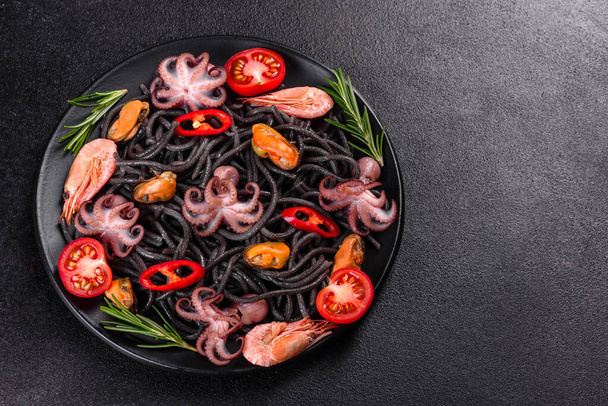 Black seafood pasta with shrimp, octopus and mussels on black background. Mediterranean gourmet food. Black pasta with octopus on a black stone plate - Photo, Image