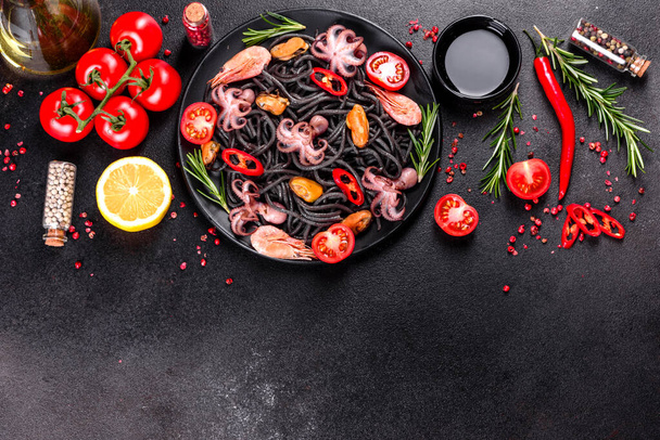 Black seafood pasta with shrimp, octopus and mussels on black background. Mediterranean gourmet food. Black pasta with octopus on a black stone plate - 写真・画像