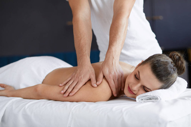 Young beautiful woman enjoying back and shouders massage in spa.Professional massage therapist is treating a female patient in apartment.Relaxation,beauty,body and face treatment concept.Home massage - Φωτογραφία, εικόνα