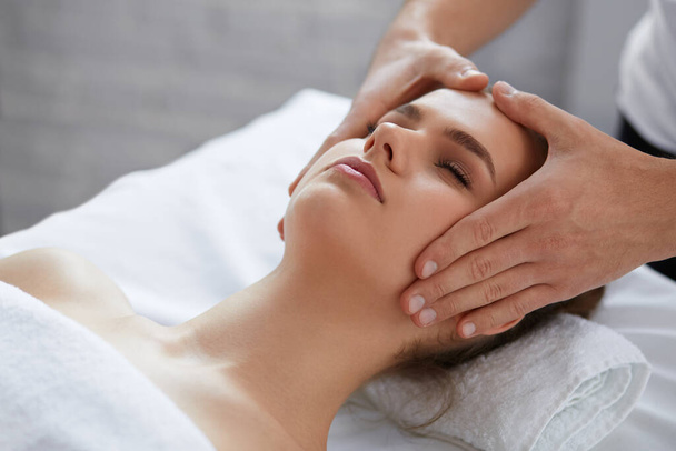 Young beautiful woman enjoying anti-aging facial massage.Male therapist making head massage to female client.Professional masseur.Relaxation,beauty,spa,body and face treatment concept - Foto, Bild