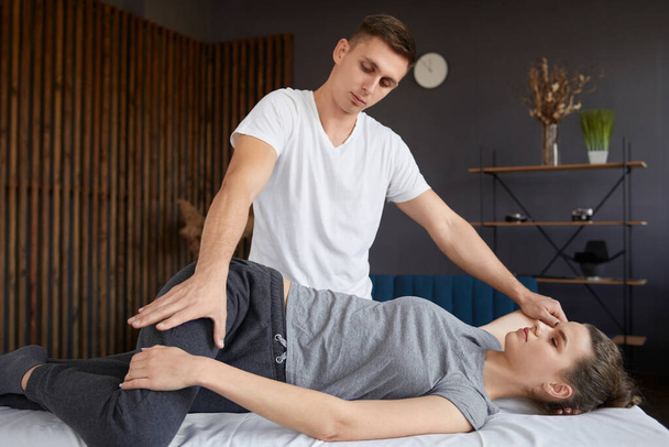 Female patient doing physical exercises with physiotherapist. Male therapist treating injured knee of young athlete.Post traumatic rehabilitation, sport physical therapy, recovery concept - Foto, Bild
