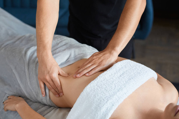 Jonge mooie vrouw genieten van anticellulite buikmassage in spa.Professionele massage therapeut is de behandeling van een vrouwelijke patiënt in appartement.Relaxatie, schoonheid, lichaamsbehandeling concept.Home massage - Foto, afbeelding