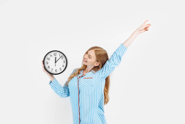 Happy cheerful girl in pajamas, holding a watch, woke up in the morning in a good mood, on a white background - Fotó, kép