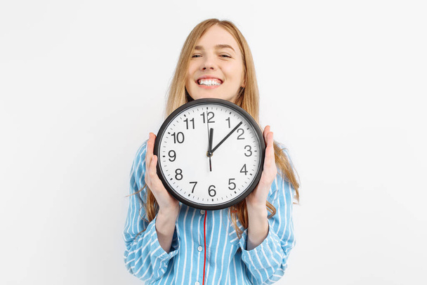Happy cheerful girl in pajamas, holding a watch, woke up in the morning in a good mood, on a white background - Foto, afbeelding