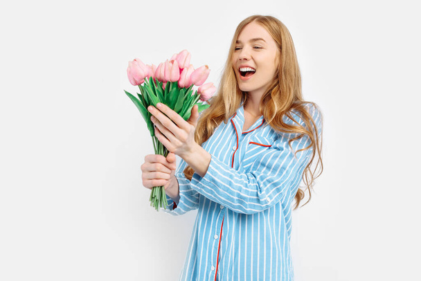 Young happy beautiful girl in pajamas holding bouquet of flowers posing on white background - Φωτογραφία, εικόνα