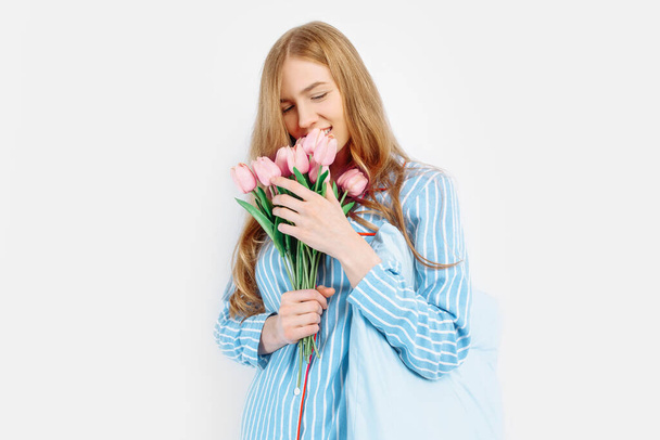 Young happy beautiful girl in pajamas holding bouquet of flowers posing on white background - Fotografie, Obrázek