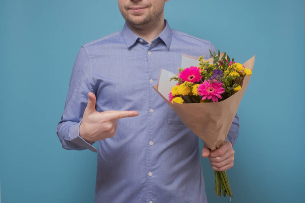 Unrecognizable man in blue shirt holding flowers as gift for his mother or girlfriend on birthday. - Photo, Image