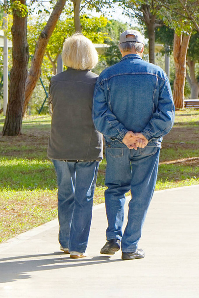 A pair of elderly people walking in the park. Elderly women and man walk in park. Back view - Zdjęcie, obraz