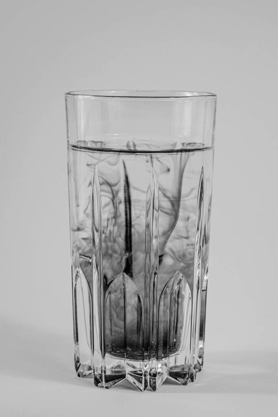 Water pollution concept. Dark substance mixing with clean water in a glass in white background - Foto, Bild