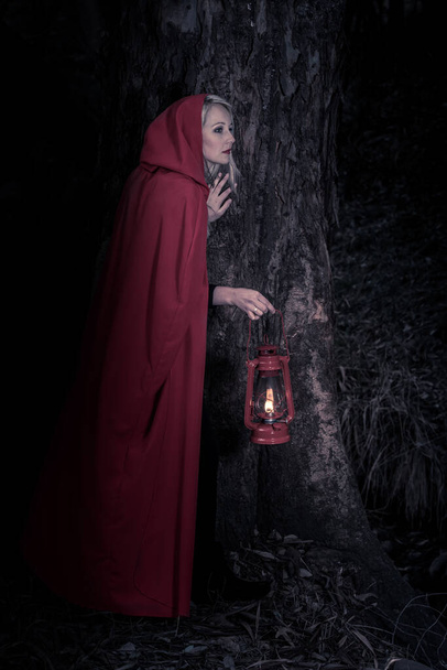 Attractive woman dressed a little red riding-hood walk in a dark forest with a lantern - Фото, зображення