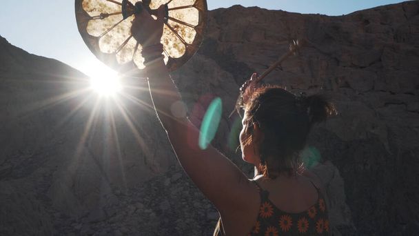 Femme méconnaissable jouant tambourin dans l'éblouissement du soleil dans les montagnes coucher de soleil
. - Photo, image