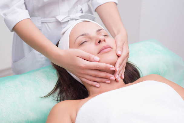Girl massage therapist does facial massage with a beautiful woman. Hands are closing. Massage room. Spa Facial treatments. Exercises for the muscles of the face. Relaxing facial massage - Φωτογραφία, εικόνα