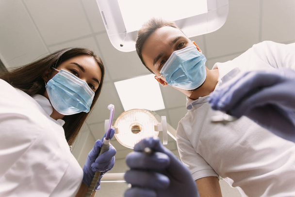 Dentist and assistant at a treatment, from the perspective of a patient. Dentist Holding Dental Tools. - Photo, image