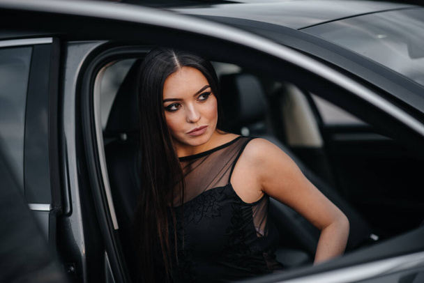 黒のドレスでビジネスクラスの車の中に座ってスタイリッシュな若い女の子。ファッション・スタイル - 写真・画像