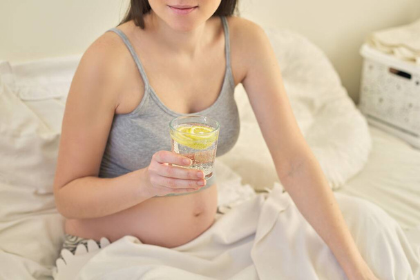 Pregnant woman drinking water with slice of lemon - Fotó, kép