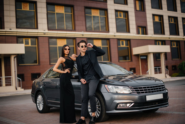 A young stylish couple in black stands near the car at sunset. Fashion and style - Foto, afbeelding