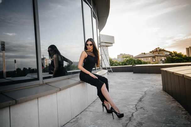 Stylish young and sexy girl posing in front of a business center in black. Fashion and style - Photo, Image