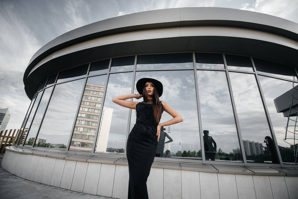 Stylish young and sexy girl posing in front of a business center in black. Fashion and style - Foto, afbeelding