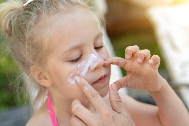 Mother applying sunscreen protection creme on cute little daughter nose face. Mom using sunblocking lotion to protect kid girl from sun during summer sea vacation. Children healthcare at travel time - Fotografie, Obrázek