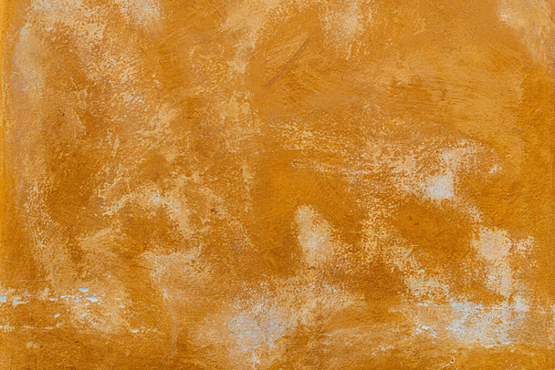 Textur einer alten, orange verputzten Straßenmauer. alte Wand mit abblätternder Farbe, zerkratzter Putz. - Foto, Bild